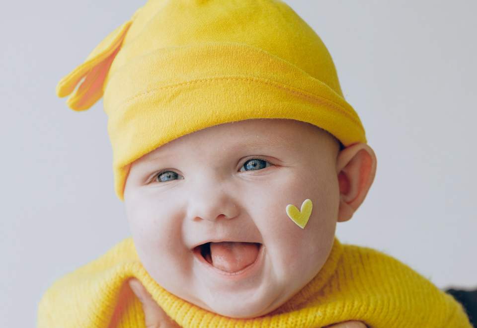 Se veria un bebe sonriendo vestido de color amarillo.